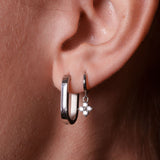 Close-up of an ear wearing a silver hoop earring with a star-shaped charm.