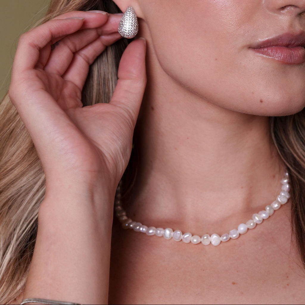 Woman wearing a pearl necklace and silver earrings against a neutral background