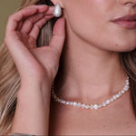 Woman wearing a pearl necklace and silver earrings against a neutral background