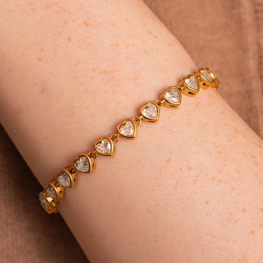 Gold bracelet with heart-shaped gemstones on a wrist against a brown background