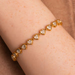 Gold bracelet with heart-shaped gemstones on a wrist against a brown background