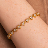 Gold bracelet with heart-shaped gemstones on a wrist against a brown background